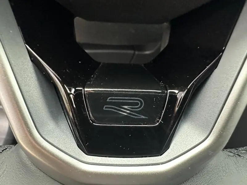 Détail du logo R sur le volant noir brillant du Volkswagen T-Roc 1.5 TSI Evo2 gris, version R-Line Edition.