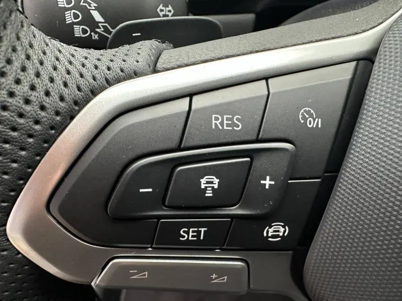 Gros plan sur les boutons de commande du régulateur de vitesse au volant cuir perforé du Volkswagen T-Roc gris.