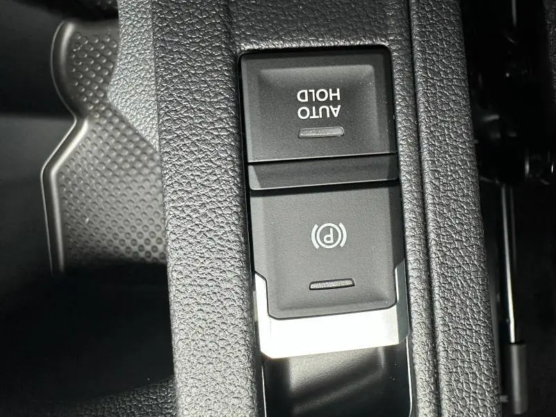 Gros plan sur le frein de stationnement électronique et bouton Auto Hold dans l'habitacle gris du Volkswagen T-Roc 2025.
