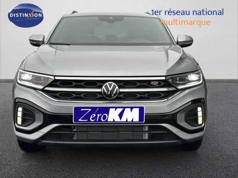 Vue frontale d'un Volkswagen T-Roc gris 2025 avec calandre R-Line et feux LED allumés.