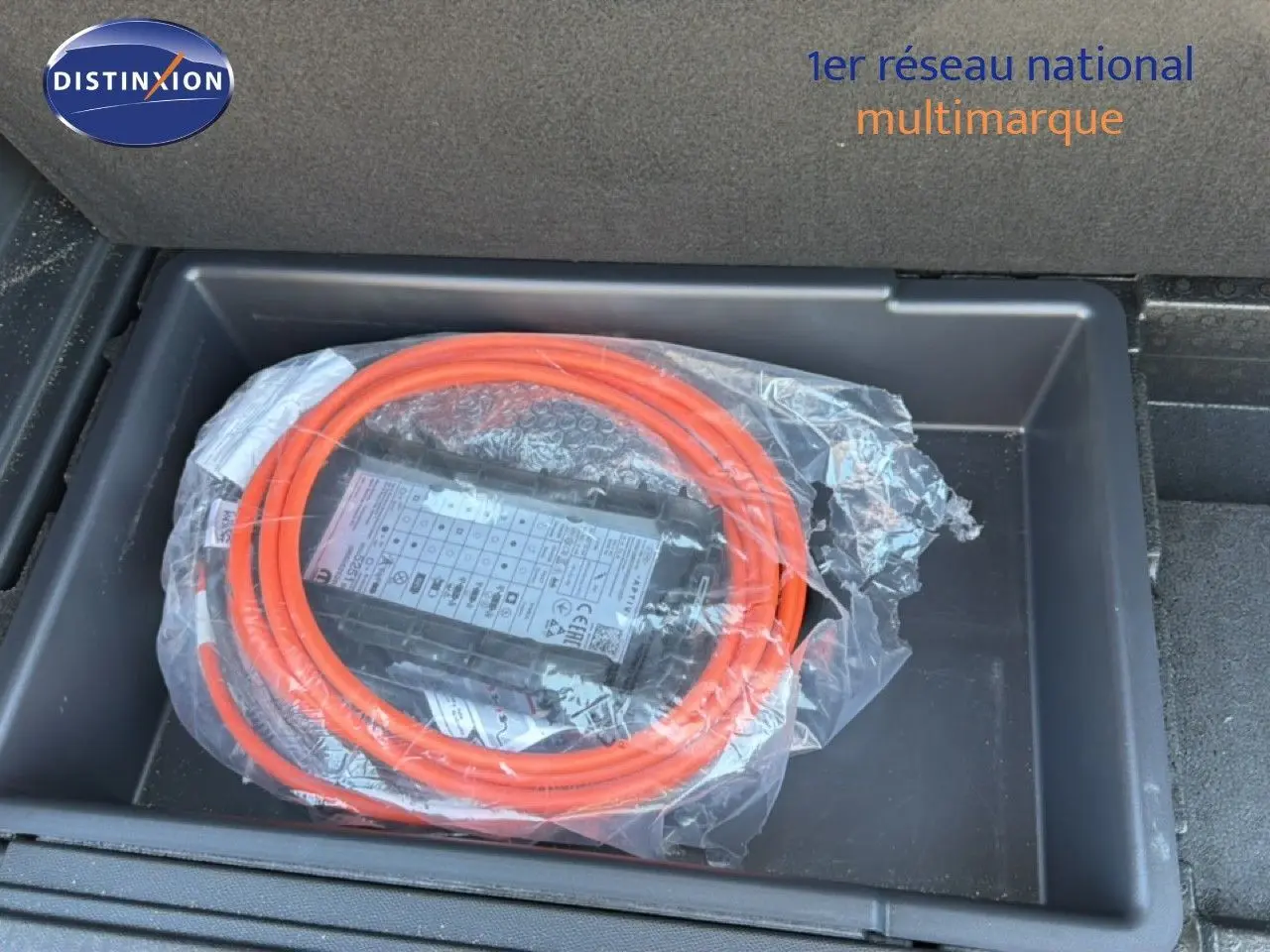 Câble de recharge hybride orange enroulé dans le coffre du Peugeot 3008 gris Artense 2024, vue plongeante.