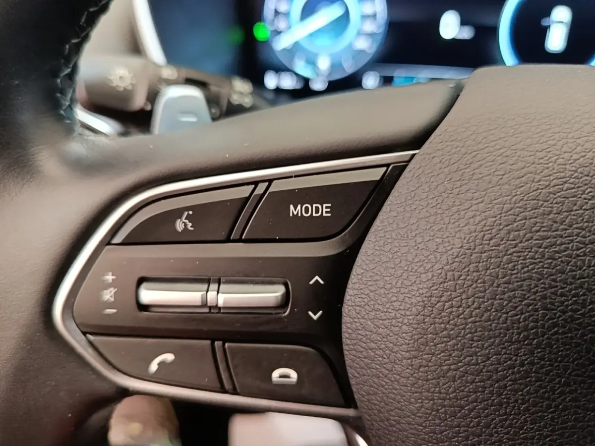 Gros plan sur les commandes gauche du volant cuir du Hyundai Santa Fe 2023, avec touches mode et volume.