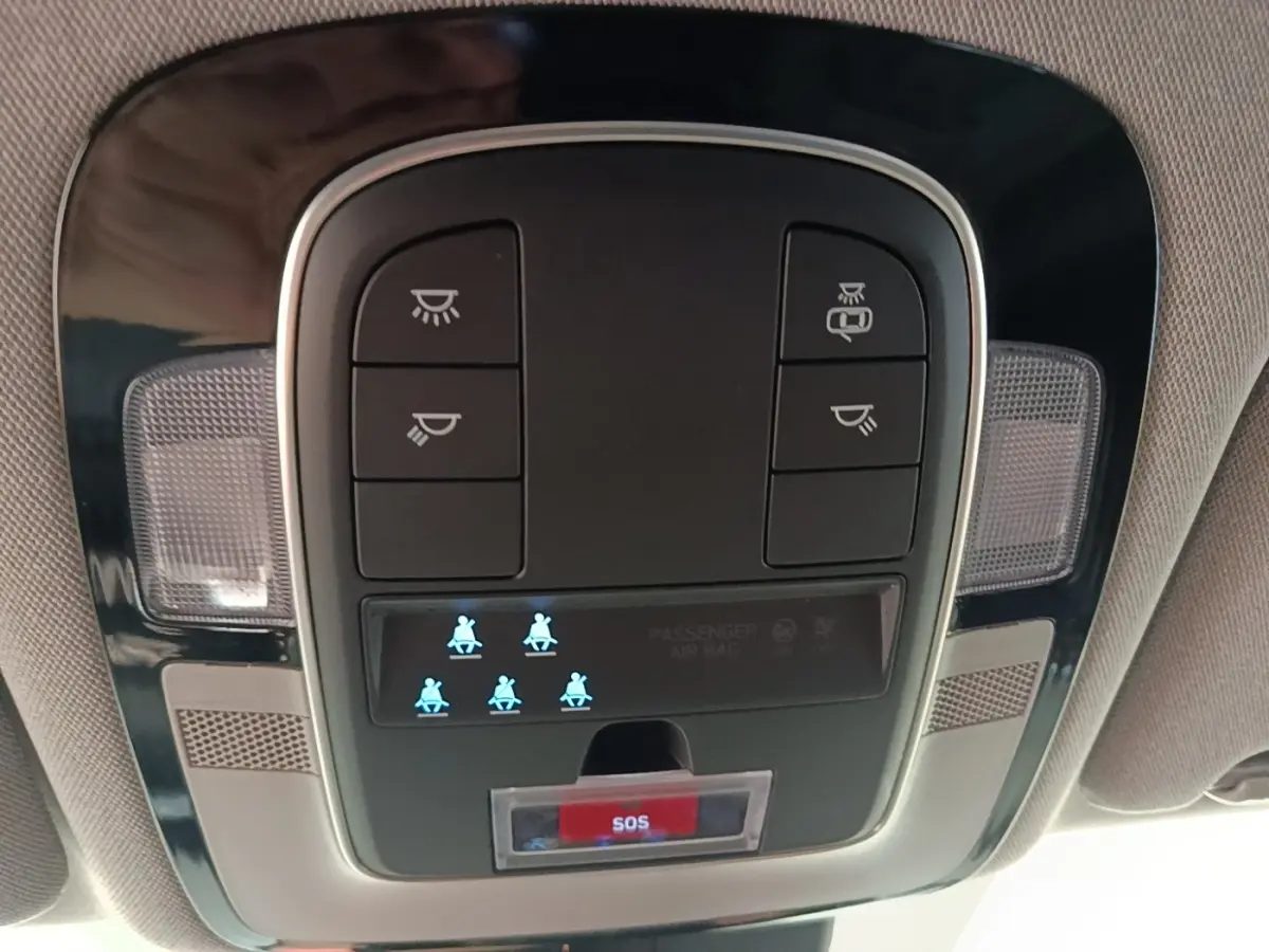 Gros plan sur la console de toit intérieure du Hyundai Santa Fe gris foncé 2023 avec bouton SOS et voyants de ceinture allumés.