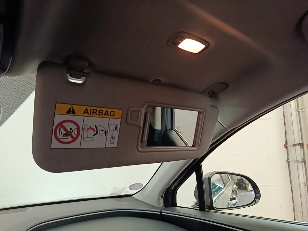 Détail intérieur du pare-soleil côté conducteur avec miroir et avertissement airbag, éclairage allumé, vue vers la portière noire.