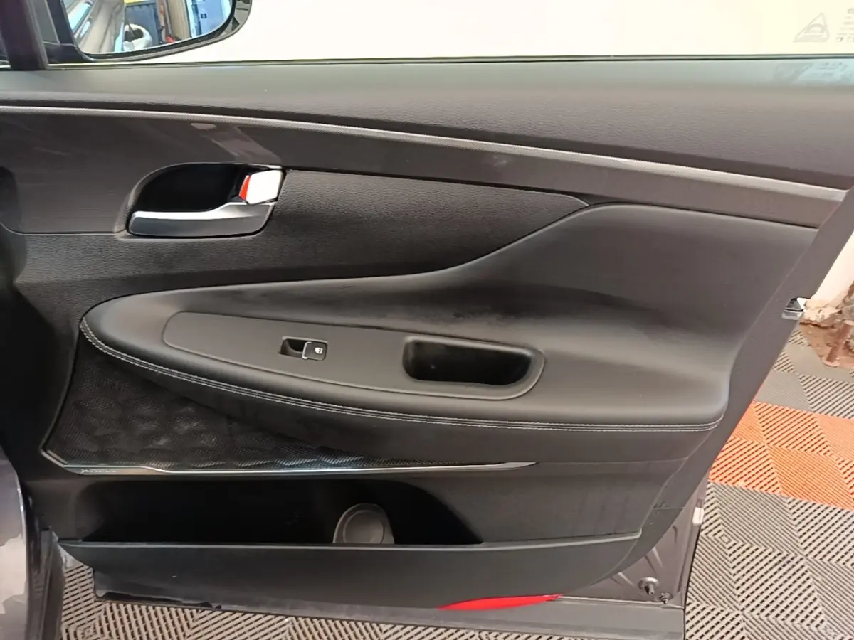 Vue rapprochée de la porte intérieure côté gauche d’un Hyundai Santa Fe gris foncé avec garniture noire et poignée chromée.