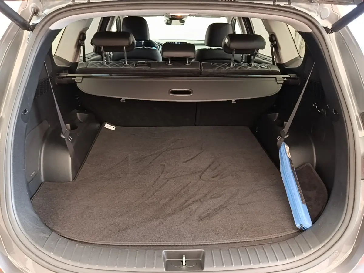 Vue intérieure du coffre ouvert du Hyundai Santa Fe gris foncé, montrant la tablette cache-bagages et les sièges arrière rabattables.