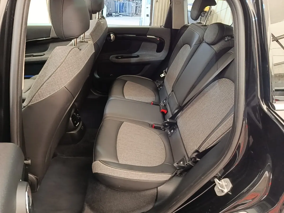 Vue côté gauche sur l'intérieur arrière du MINI Countryman noir 2023, sièges tissu et cuir bicolores avec ceinture grise.