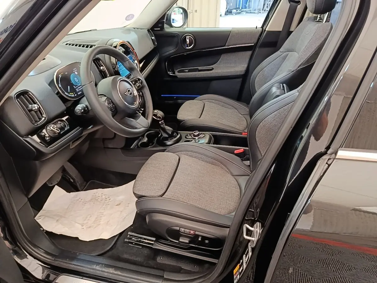 Vue intérieure côté conducteur du MINI Countryman noir 2023, sièges tissu gris et volant cuir multifonctions.