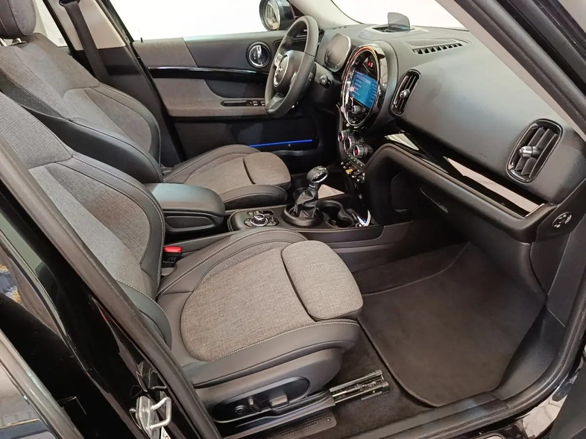 Vue intérieure côté conducteur du MINI Countryman noir 2023, sièges tissu et cuir, tableau de bord avec écran tactile.