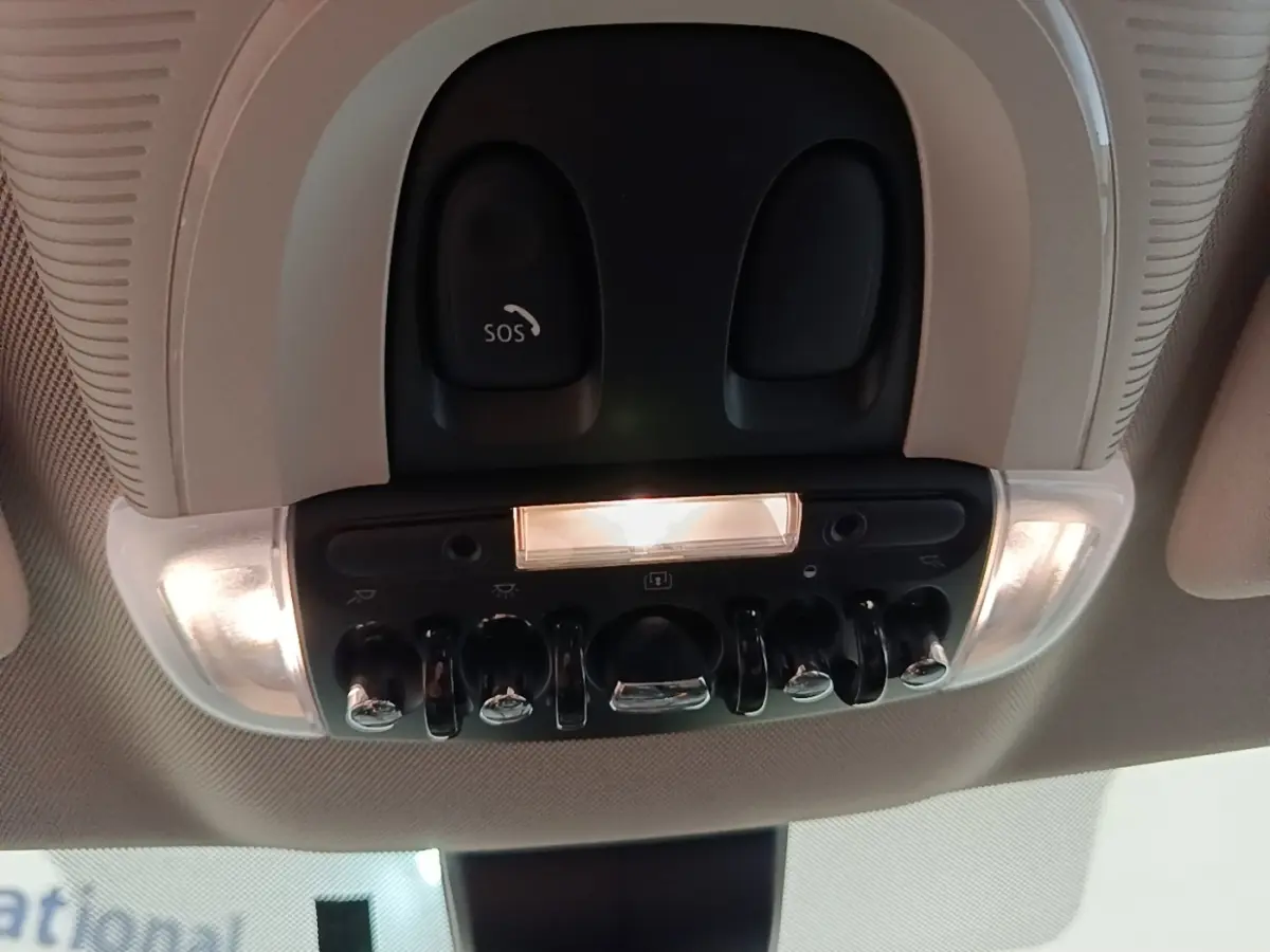Vue intérieure en contre-plongée du plafonnier noir avec interrupteurs chromés et bouton SOS éclairé d'une MINI Countryman 2023.