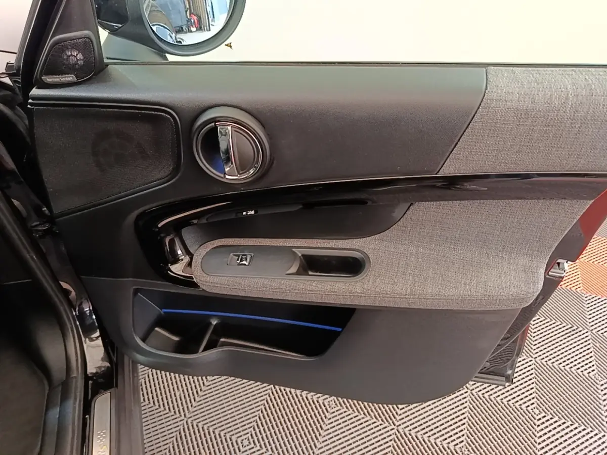 Intérieur de la porte avant gauche noire du MINI Countryman 2023 avec habillage tissu gris et éclairage d’ambiance bleu.