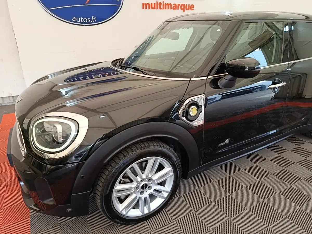 Vue 3/4 avant droit d'une MINI Countryman hybride noire avec jantes argentées et logo électrique sur l'aile.