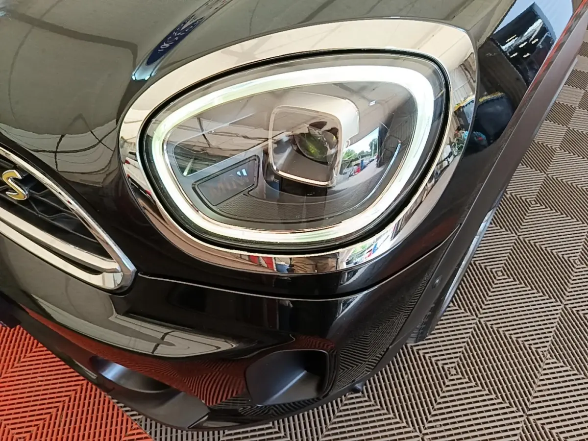 Gros plan sur le phare avant droit LED d'une MINI Countryman Cooper SE noire, avec calandre et logo "S" visibles.