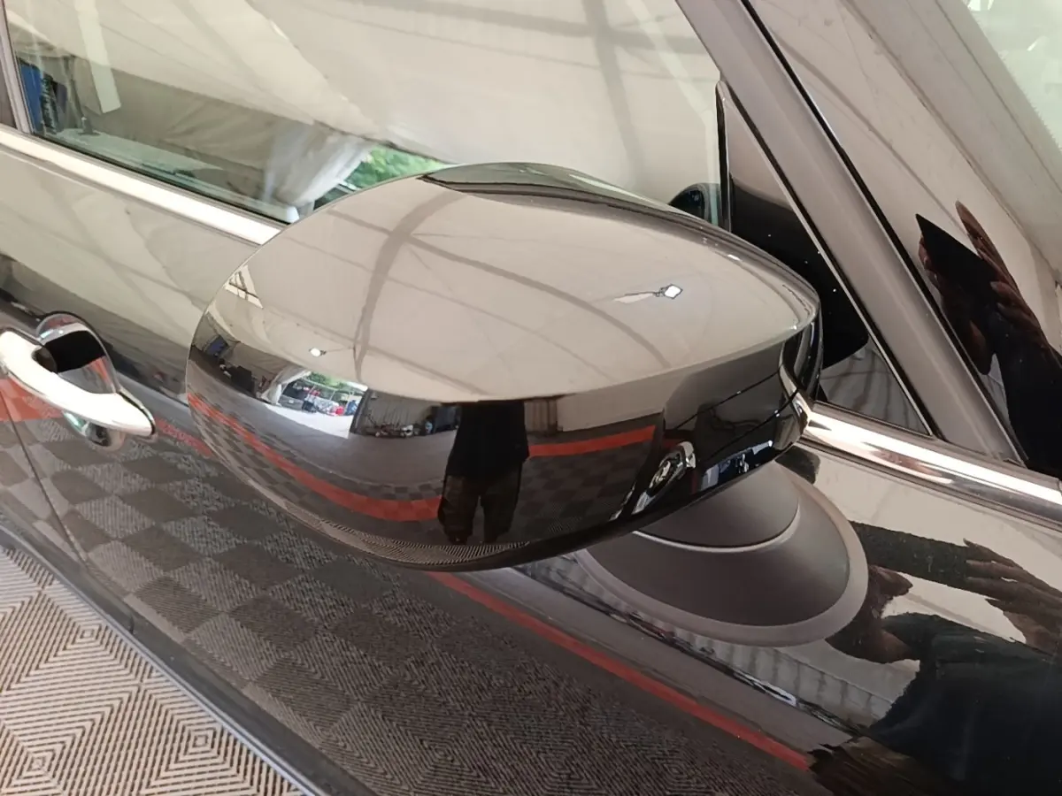 Gros plan sur le rétroviseur droit noir brillant du MINI COUNTRYMAN Cooper SE 2023, reflétant l'environnement intérieur.