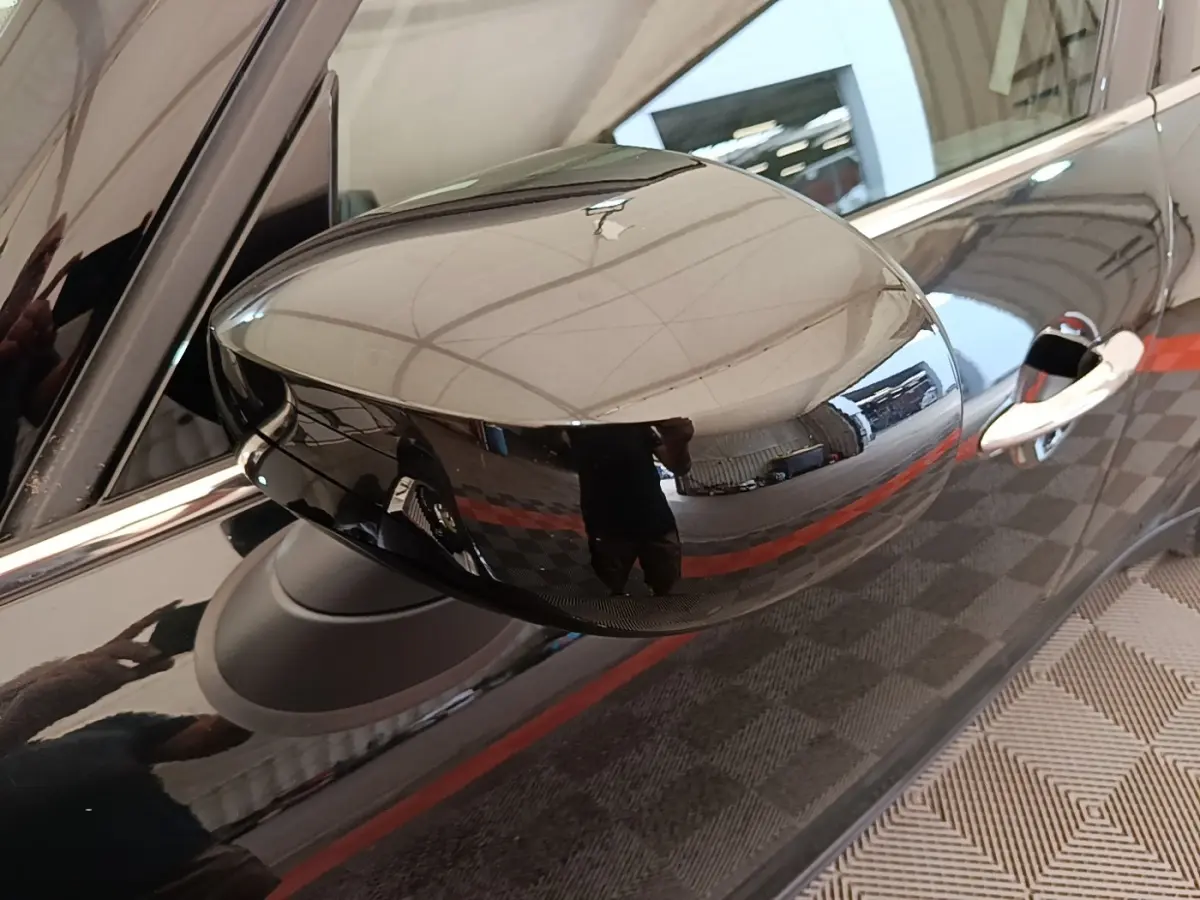 Gros plan sur le rétroviseur droit noir brillant d'un MINI Countryman 2023, reflet de l'environnement intérieur visible.