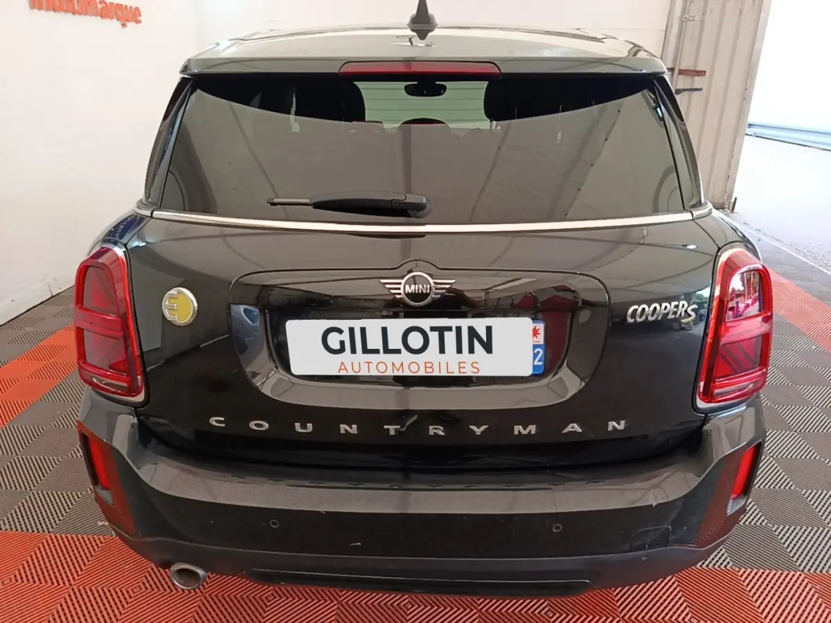 Vue arrière d'une MINI Countryman Cooper SE noire avec logo hybride jaune sur le côté gauche du coffre.