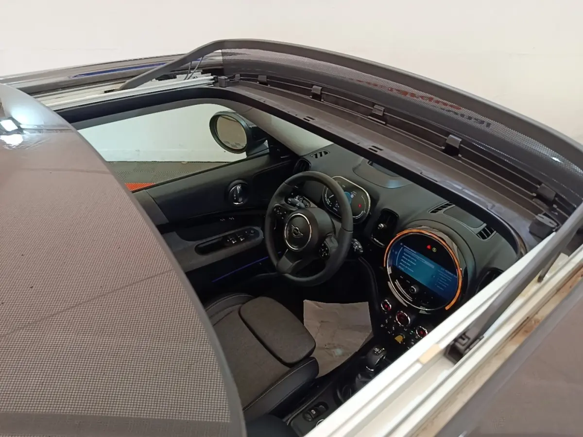 Vue intérieure du MINI Countryman Cooper SE 2023 noir, toit ouvrant électrique ouvert, tableau de bord et volant cuir visibles.