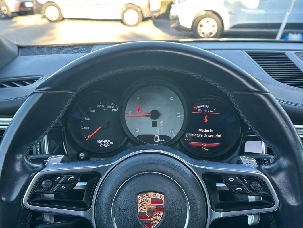 Vue rapprochée du tableau de bord et volant cuir noir du Porsche Macan gris foncé, affichant le compteur et alertes.