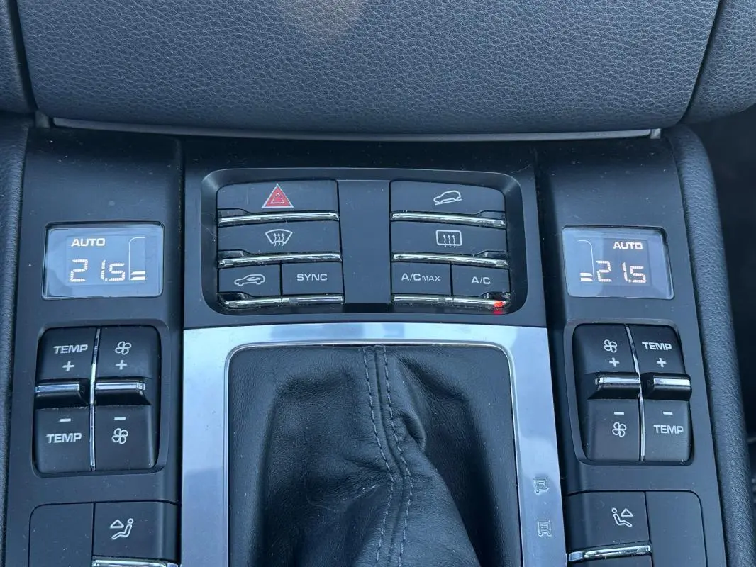 Vue rapprochée de la console centrale du Porsche Macan gris foncé, montrant les commandes de climatisation automatique et les boutons de réglage.