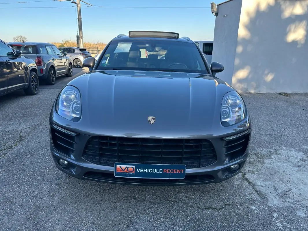 Vue avant d'un Porsche Macan gris foncé 2015 avec toit panoramique et calandre noire, stationné en extérieur.
