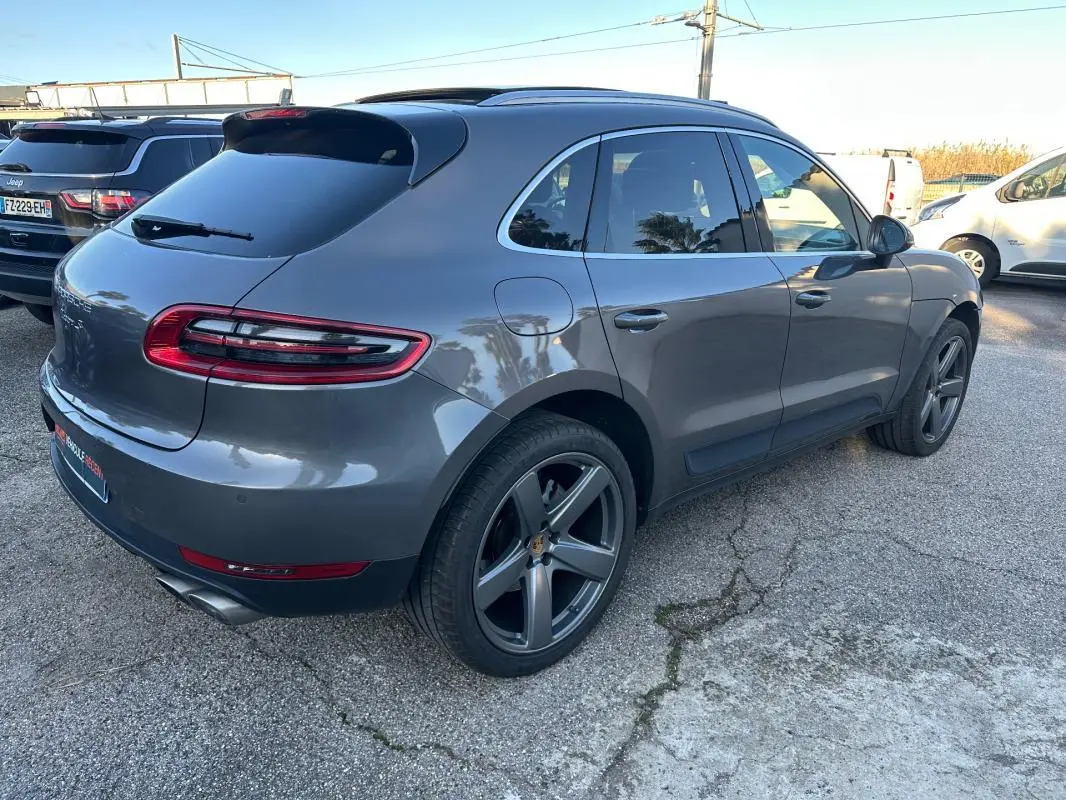 Vue 3/4 arrière droite d'un Porsche Macan gris foncé avec jantes 18 pouces et toit panoramique visible.
