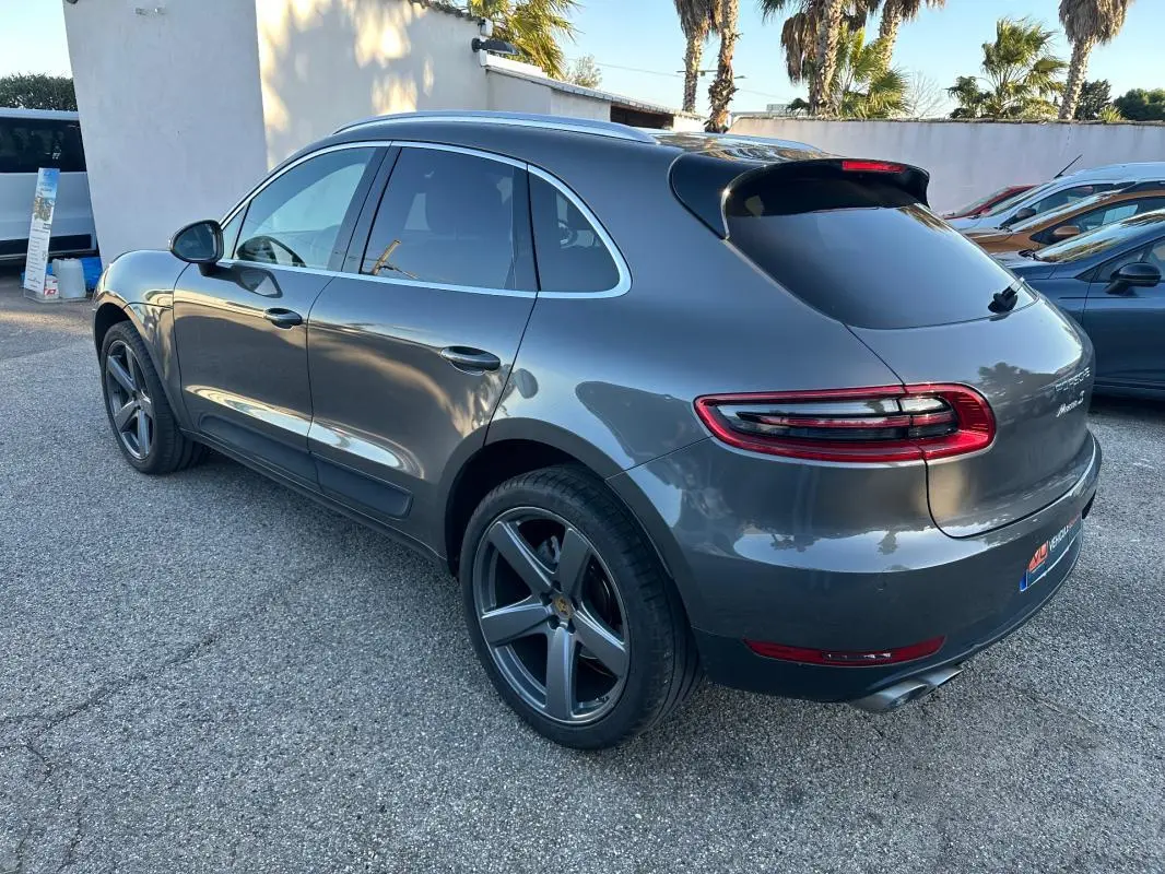 Vue 3/4 arrière droite d'un Porsche Macan gris foncé avec jantes 18 pouces et vitres teintées.