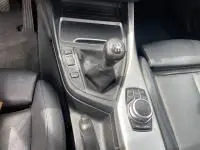 Gros plan sur la console centrale d'une BMW Série 1 M Sport blanche de 2018, montrant le levier de vitesse manuel et le contrôleur iDrive.