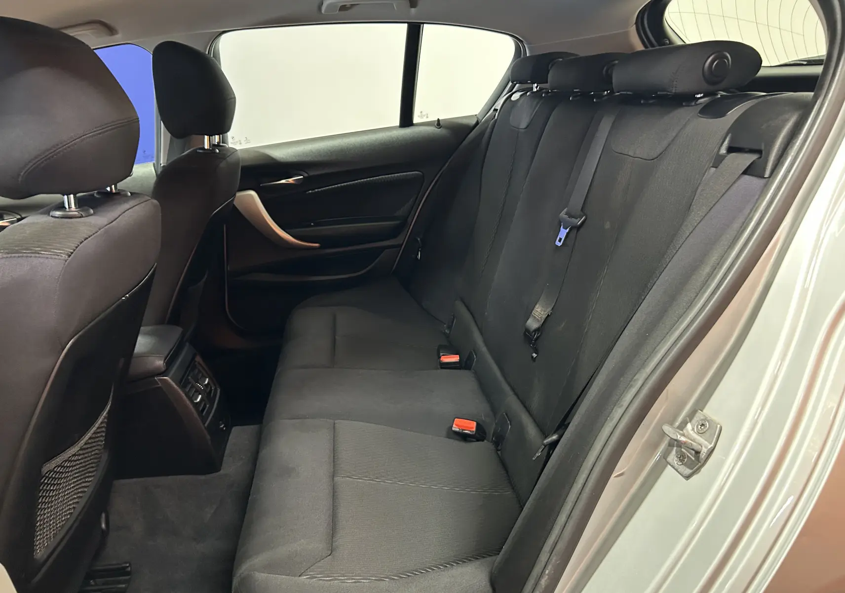 Vue intérieure arrière côté droit de la BMW Série 1 gris, montrant les sièges en tissu noir et les appuie-têtes.