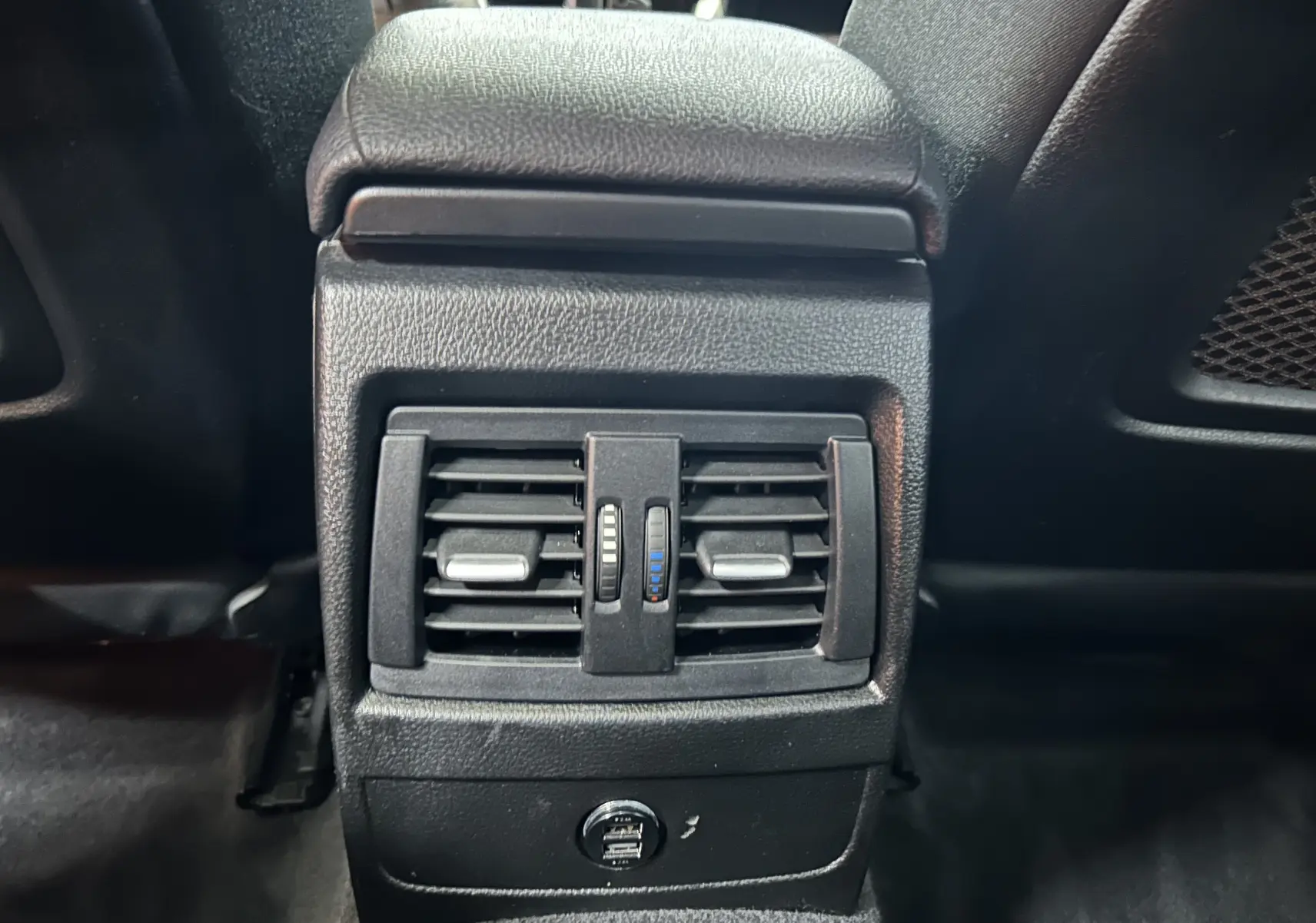 Gros plan sur la console arrière noire avec bouches d'aération et ports USB de la BMW Série 1 gris 2014.