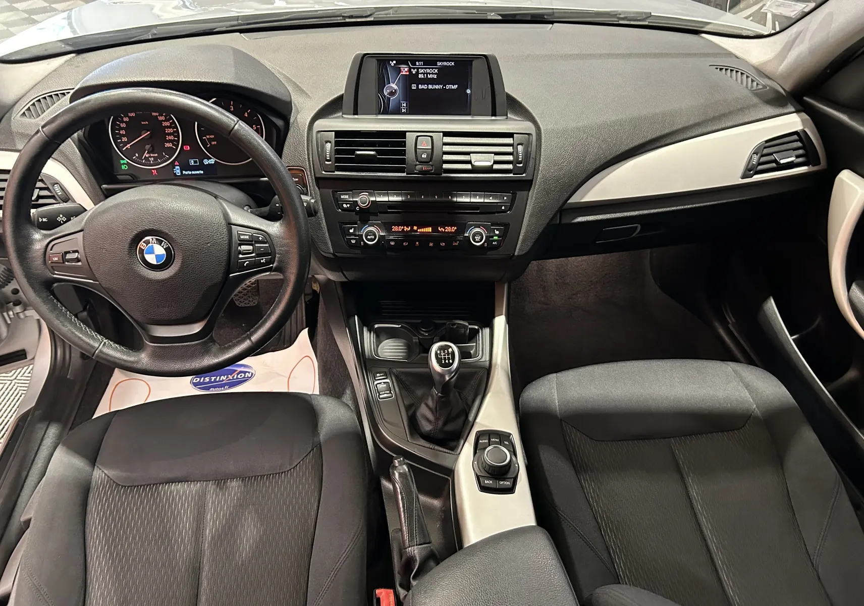 Intérieur BMW Série 1 gris 2014, vue frontale du tableau de bord avec volant, console centrale et sièges tissu noirs.