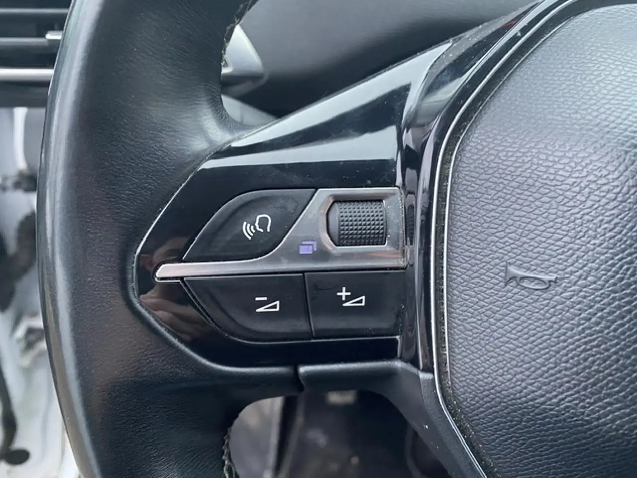 Gros plan sur les commandes gauche du volant noir du Peugeot 3008 blanc, avec boutons de volume et appel mains-libres.