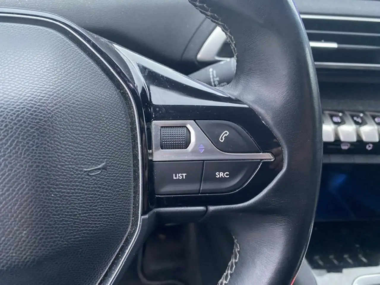 Gros plan sur les commandes au volant noir du Peugeot 3008 blanc, version Allure 2017, avec tableau de bord en arrière-plan.