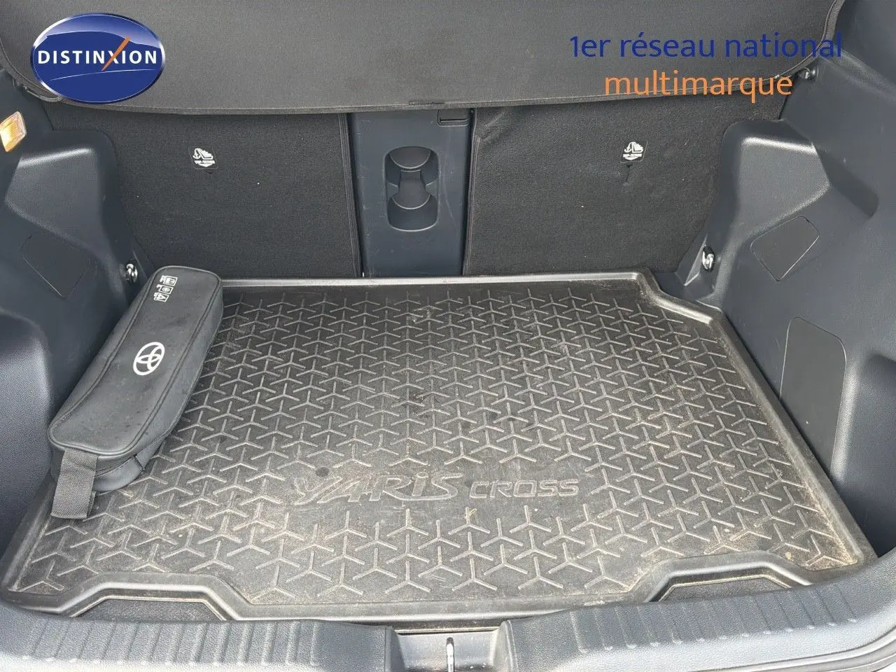 Coffre ouvert d'une Toyota Yaris Cross gris minéral, avec tapis de coffre marqué Yaris Cross et rangement latéral Toyota.