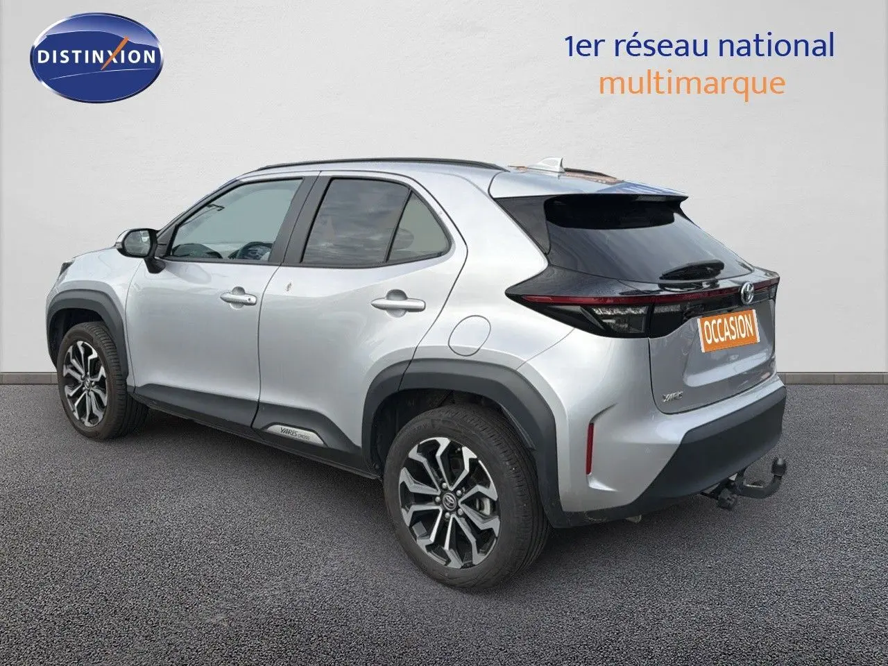 Toyota Yaris Cross gris minéral vue 3/4 arrière droit avec jantes bi-ton et attelage visible.