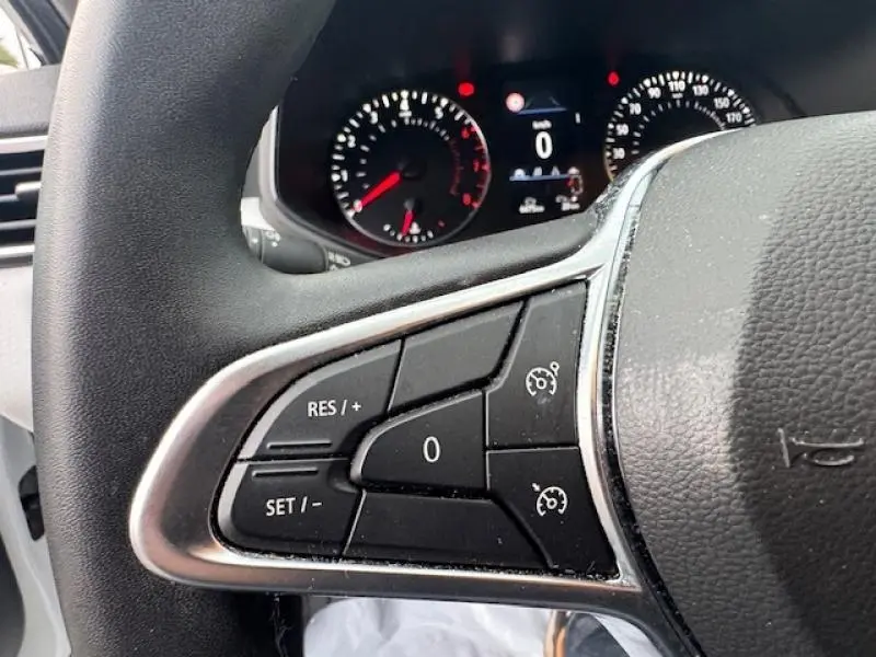 Gros plan sur les commandes du régulateur de vitesse au volant d'une Renault Clio blanc glacier, tableau de bord en arrière-plan flou.