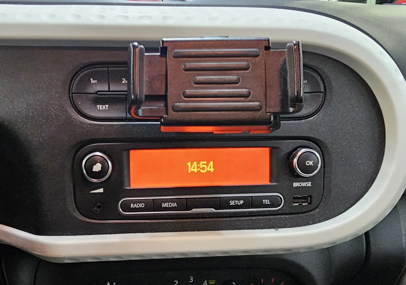 Gros plan sur la console centrale de la Renault Twingo III gris lunaire, affichant l'horloge digitale à 14h54.