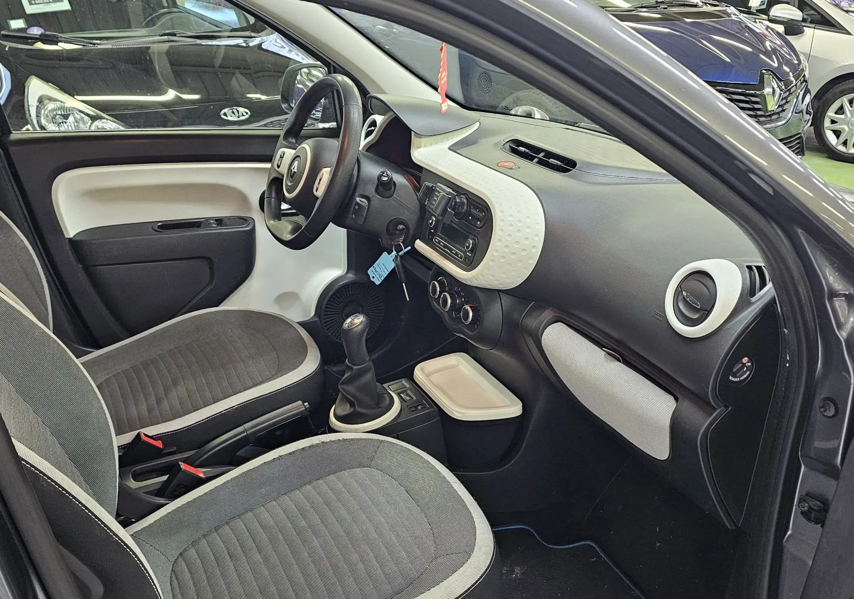 Intérieur avant droit d'une Renault Twingo III gris lunaire, avec tableau de bord bicolore et boîte manuelle visible.