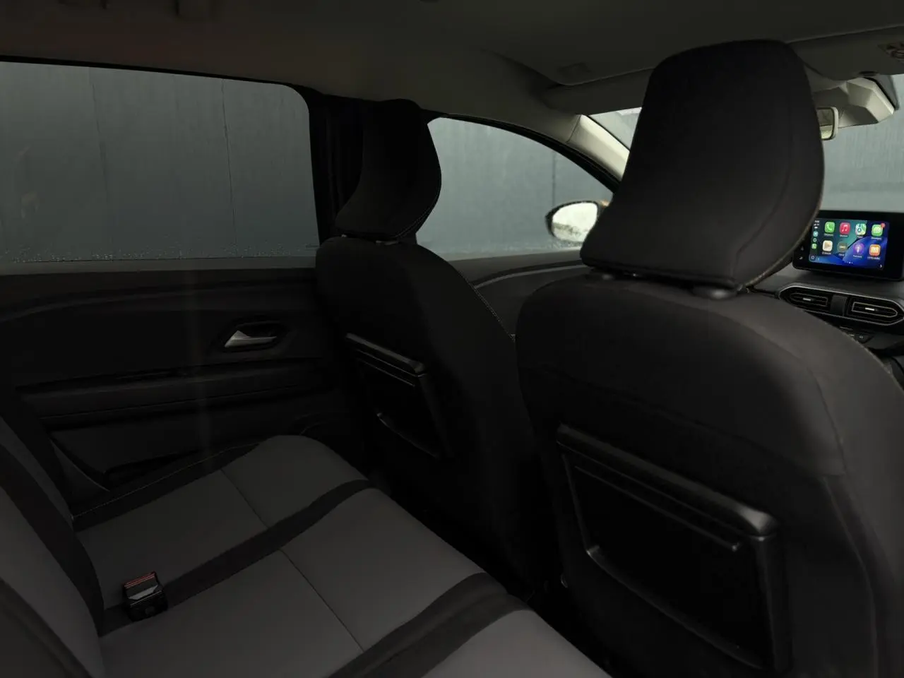 Vue intérieure arrière du Dacia Jogger gris urbain, montrant les sièges et l'écran tactile du tableau de bord.