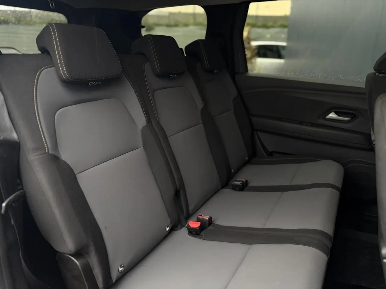 Vue intérieure du rang 2 des sièges gris du Dacia Jogger 1.6 Hybrid 140 Extreme 7 places, avec appuie-têtes et ceintures visibles.