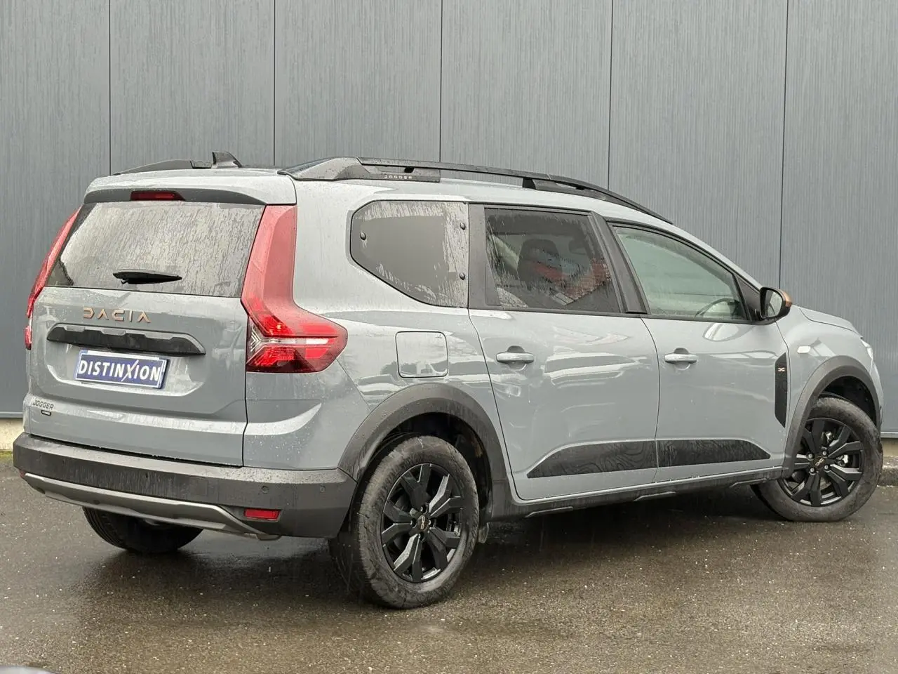 Vue 3/4 arrière droite d'un Dacia Jogger gris urbain avec jantes noires et barres de toit modulaires.