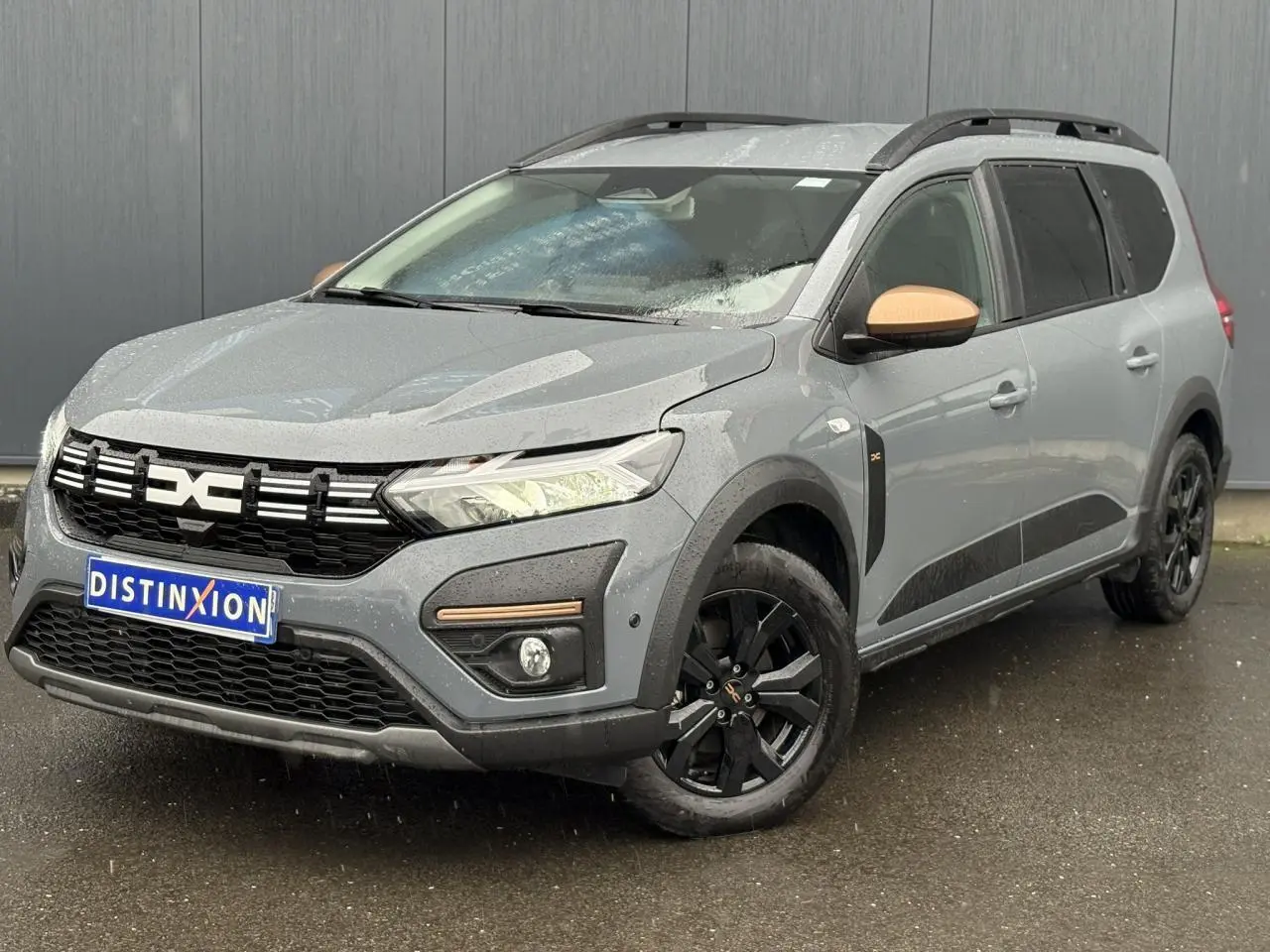 Vue 3/4 avant d'un Dacia Jogger gris urbain avec jantes noires et coques de rétroviseurs couleur cuivre.