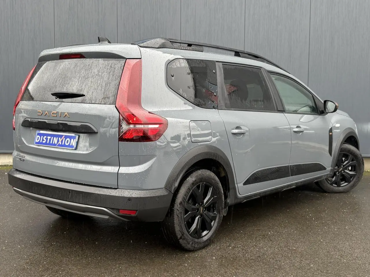 Vue 3/4 arrière droite du Dacia Jogger gris urbain 2025 avec jantes noires et barres de toit longitudinales.