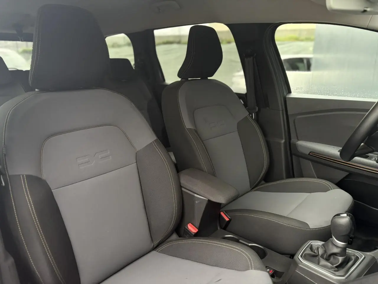 Vue intérieure des sièges avant gris clair et foncé du Dacia Jogger 1.6 Hybrid 140 Extreme avec accoudoir central et levier de vitesse.