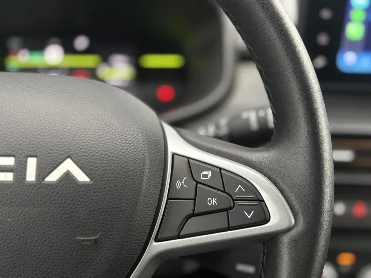 Gros plan sur le volant côté droit du Dacia Jogger gris urbain avec commandes multifonctions et tableau de bord flou.
