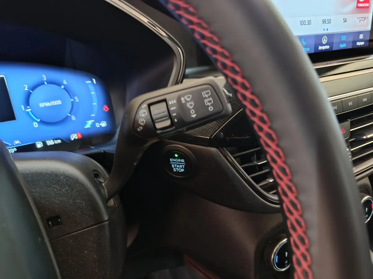 Gros plan intérieur sur le volant cuir noir avec surpiqûres rouges et tableau de bord digital bleu du Ford Kuga 2024.