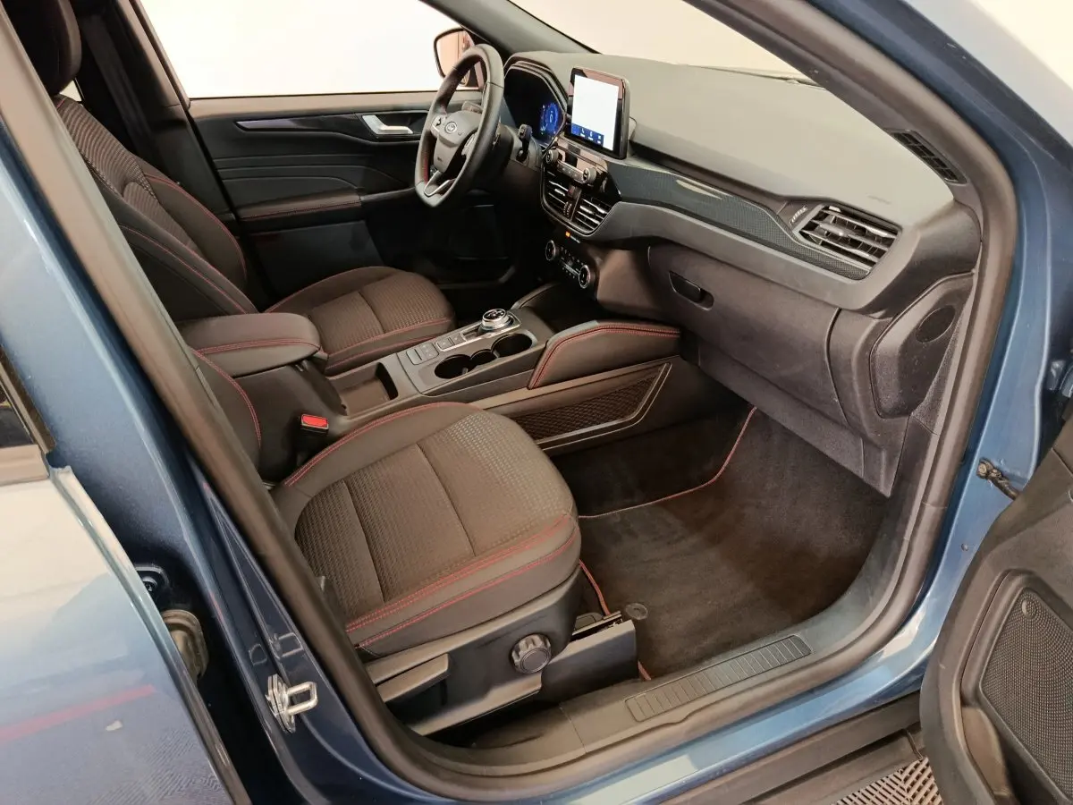Intérieur avant droit du Ford Kuga bleu 2024, sièges noirs avec surpiqûres rouges et écran tactile central.