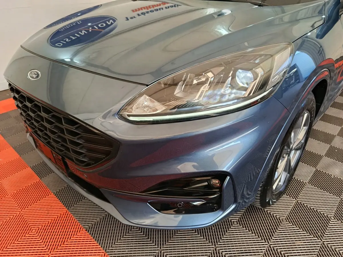 Vue 3/4 avant droit du Ford Kuga bleu 2024, mettant en valeur le phare LED et la calandre noire sportive.