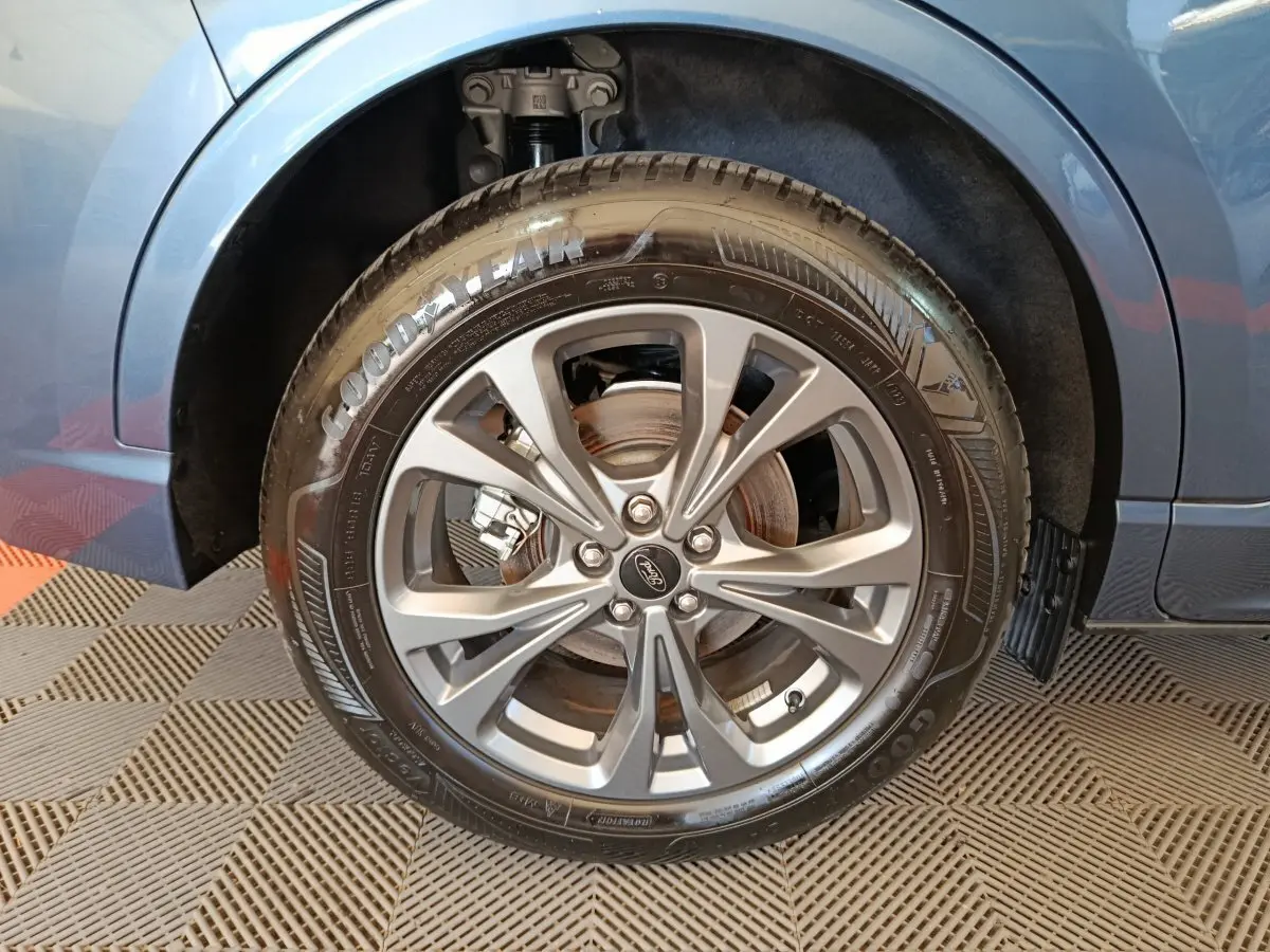 Gros plan sur la roue avant droite du Ford Kuga bleu 2024, avec jante alliage et pneu Goodyear visible.