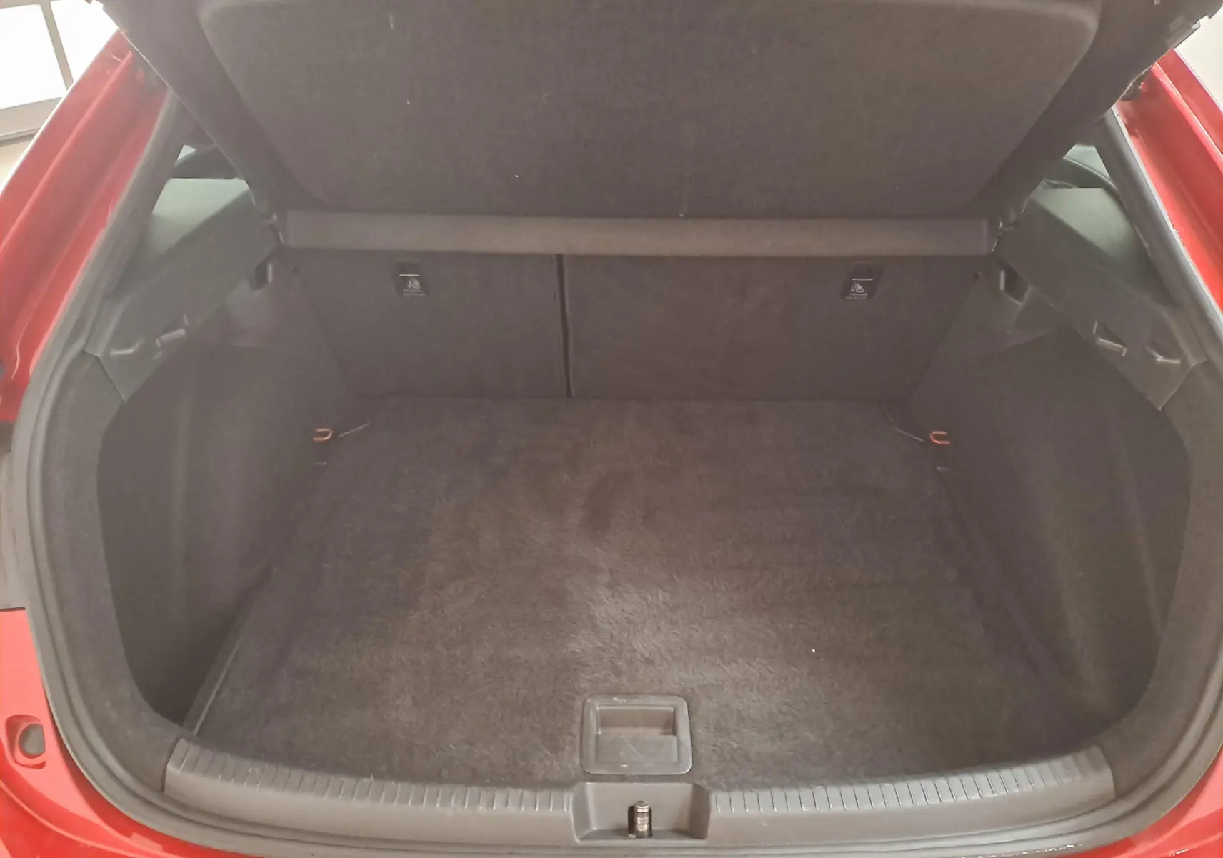 Coffre ouvert d’un Volkswagen Taigo Rouge Roi, vue plongeante sur l’espace de chargement vide et tapis noir.