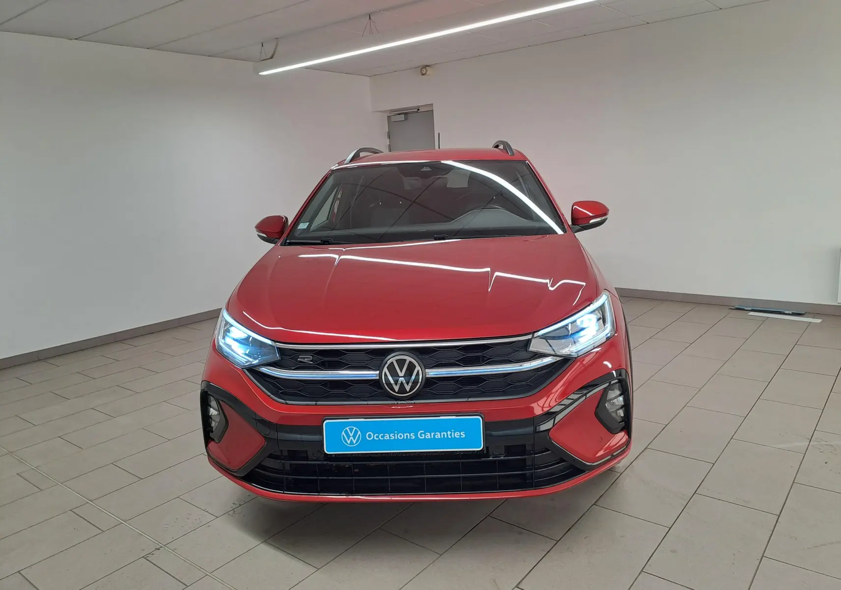 Vue frontale d'un Volkswagen Taigo Rouge Roi 2021 avec phares allumés et calandre R-Line noire brillante.